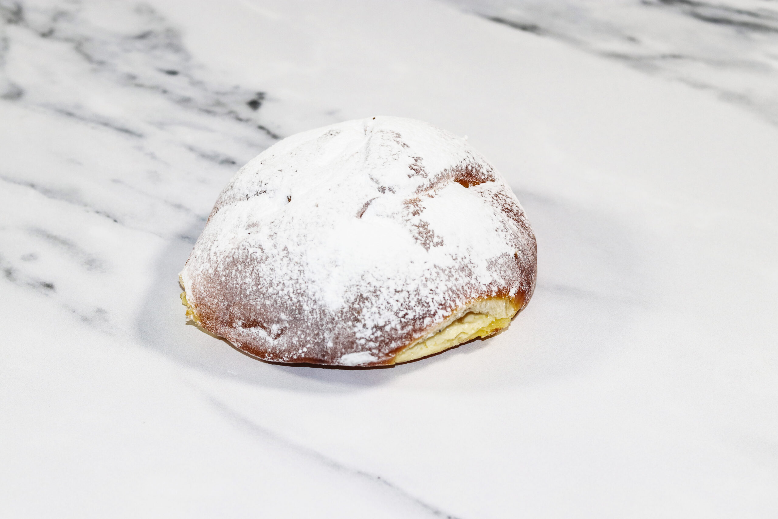 Powdered sugar donut resting on a white marble surface.